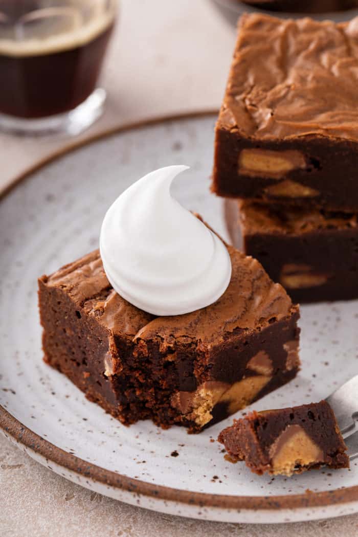 Plated peanut butter cup brownie topped with whipped cream, with a fork taking a bite from the corner.