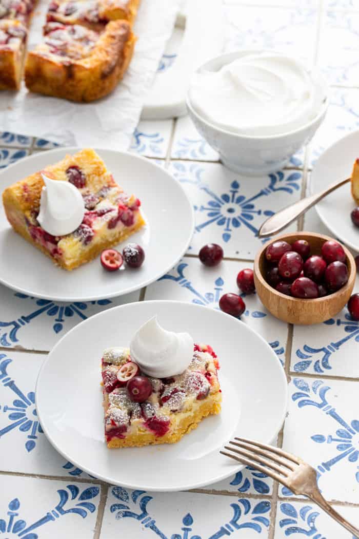 White plates with pieces of whipped-cream-topped gooey butter bars. one bar has a bite taken out of the corner