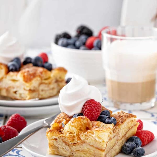 Two plates with slices of croissant bread pudding, topped with whipped cream and fresh berries