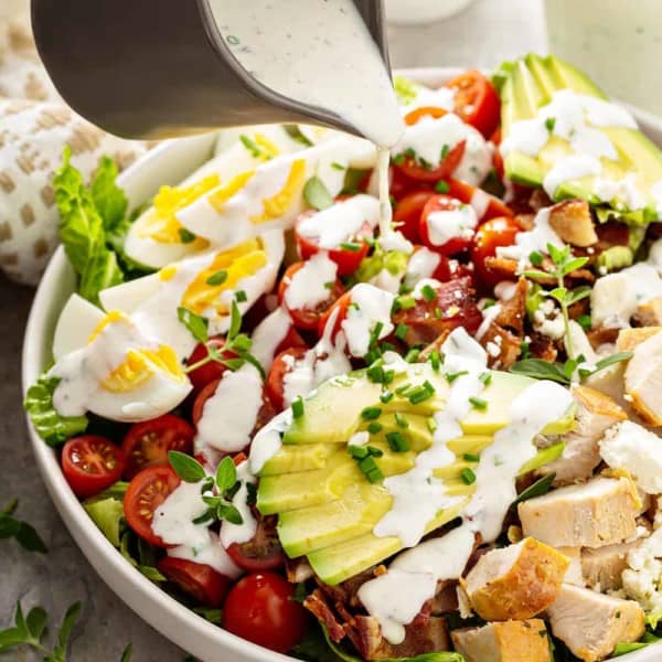 Ranch dressing being poured over the top of a cobb salad