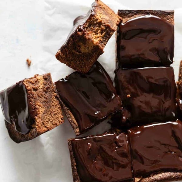 Sliced pumpkin blondies topped with chocolate ganache, with two turned on the side to show pumpkin swirl