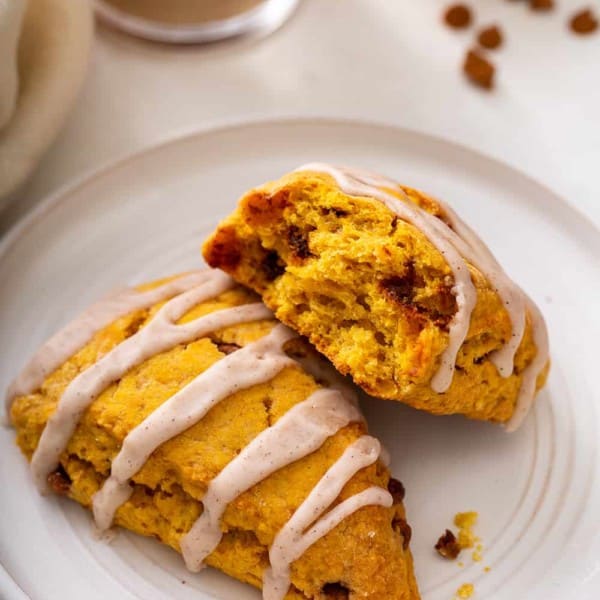 Two pumpkin scones on a white plate. One of them has been broken in half to show the inside of the scone