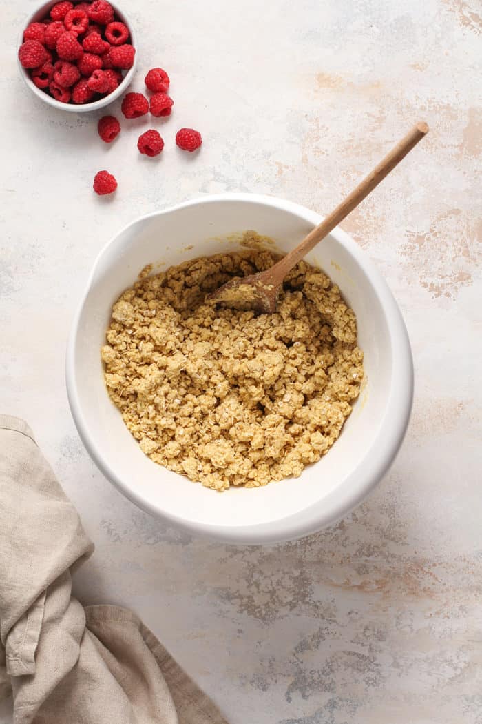 Wooden spoon stirring the crumble base for raspberry bars in a white mixing bowl