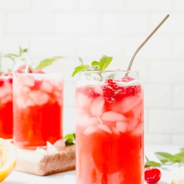 Glass of raspberry lemonade with a sprig of mint and a metal straw in the foreground, with 2 more glasses of lemonade in the background