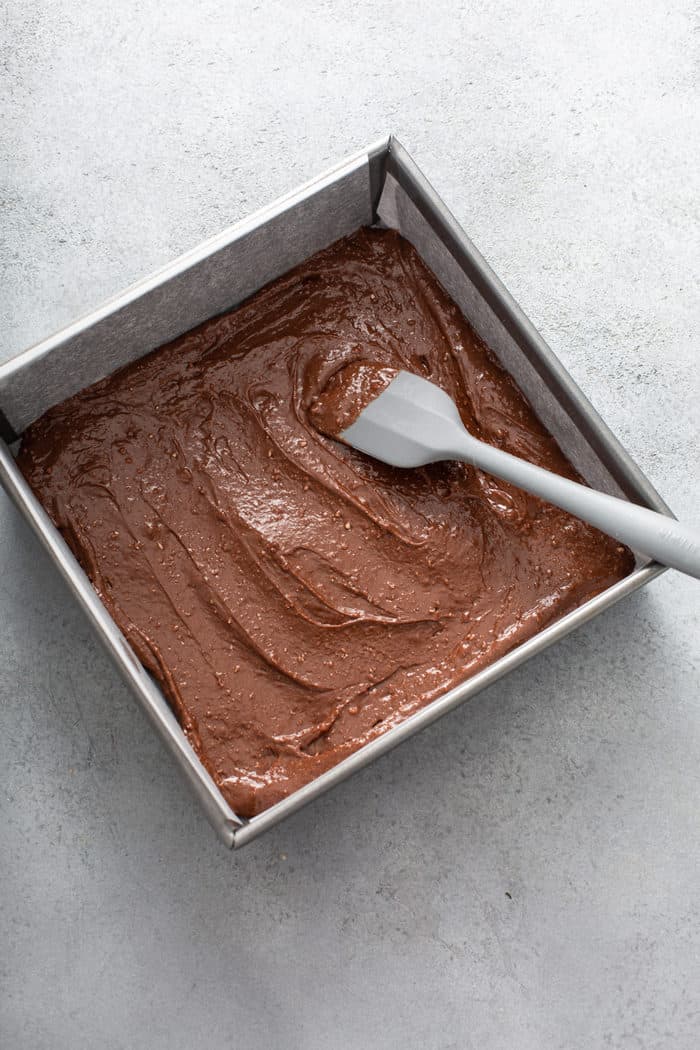 Spatula spreading salted caramel brownie batter into a metal baking pan