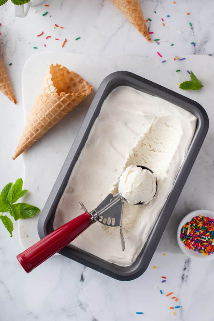 Ice cream scoop scooping out vanilla no-churn ice cream from a container.