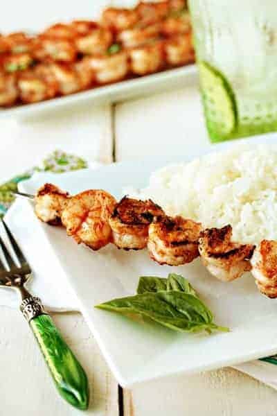 Marinated grilled shrimp on a skewer next to white rice on a plate