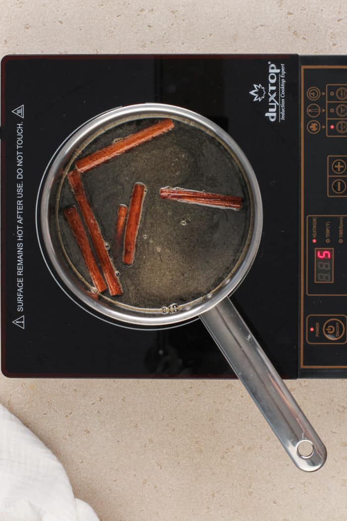 Brown sugar syrup coming to a simmer in a saucepan on a burner.