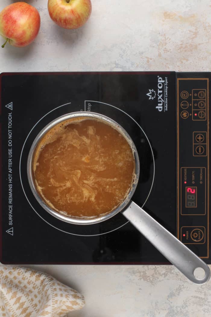 Apple cider being simmered and reduced in a saucepan on a burner.