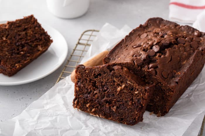 Loaf of chocolate zucchini bread on a piece of parchment paper. A slice has been cut from the end of the loaf.