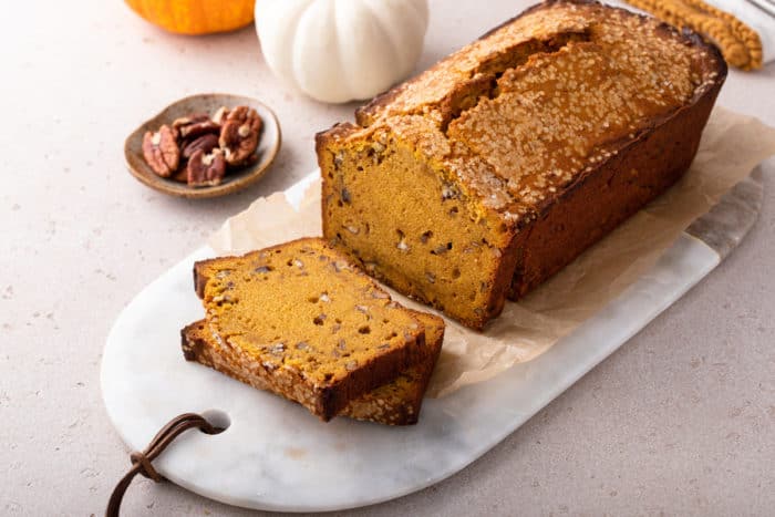 Loaf of brown butter pumpkin bread with several slices cut from it set on a marble board.