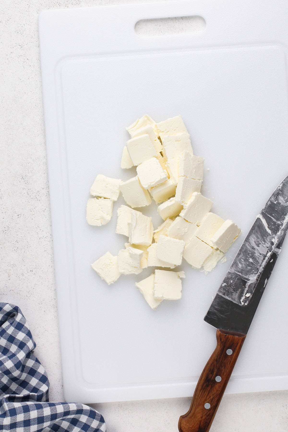 Cream cheese cut into squares on a white cutting board.