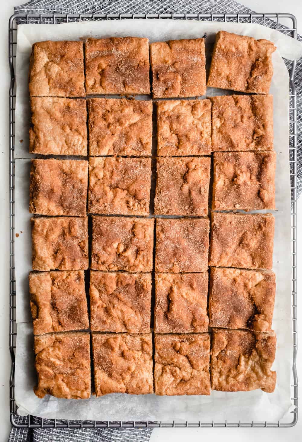 Baked and cut snickerdoodle blondies in a parchment-lined cooling rack