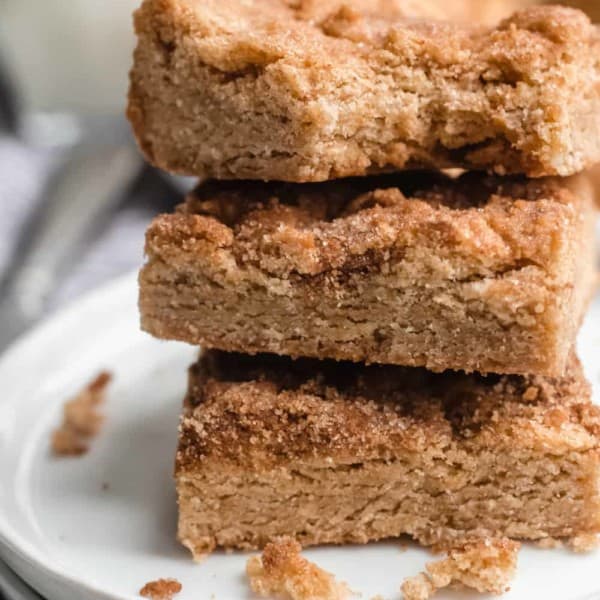 Three stacked snickerdoodle blondies on a white plate. The top blondie has a bite taken out of it.