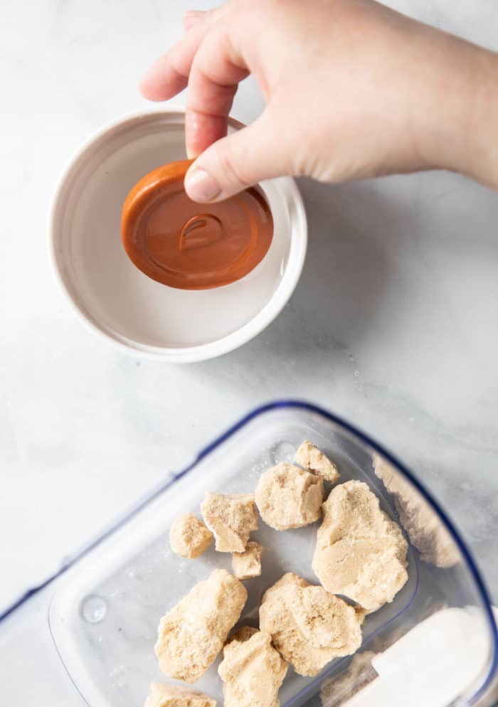 Hand placing a disk of terra cotta in a bowl of water next to a container with hard brown sugar lumps in it.