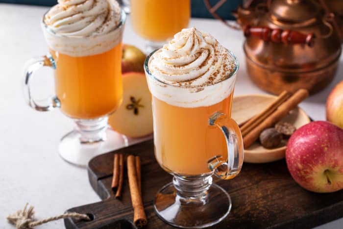 Mug of spiced apple cider on a wooden board. Two more mugs of cider are visible in the background.