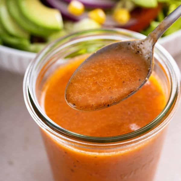 Spoon holding up a spoonful of chipotle vinaigrette over a jar of the dressing.