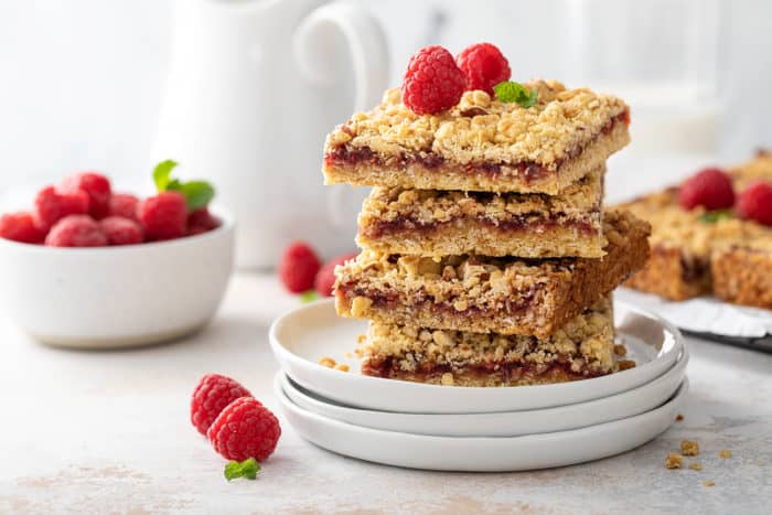 Four raspberry bars stacked on top of a white plate