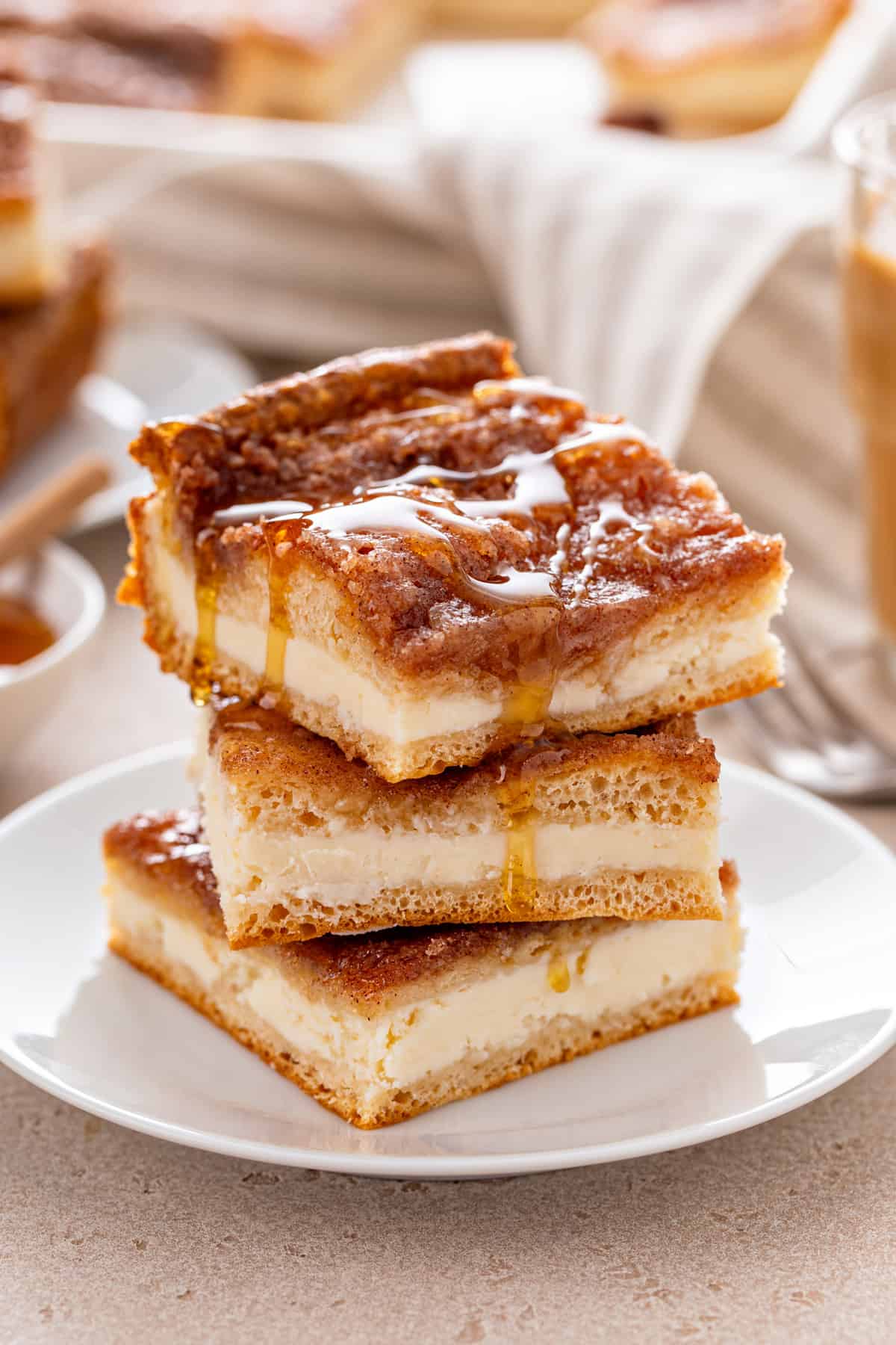 Three slices of sopapilla cheesecake stacked on a white plate, with honey drizzled on top.