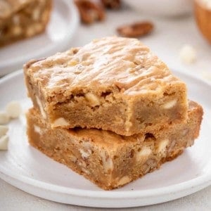 White plate with two white chocolate pecan blondies stacked on it.