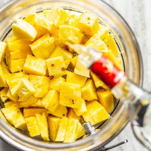 Vodka being poured over diced pineapple in a glass container