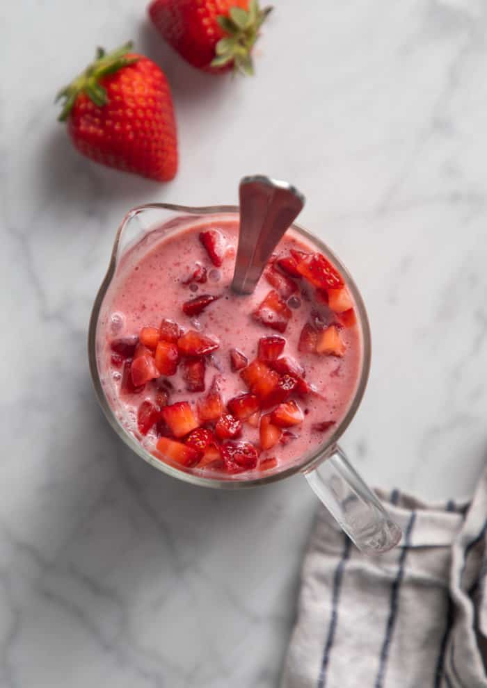 Diced strawberries being added to strawberry popsicle base in a large measuring cup.