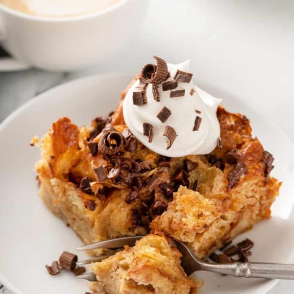 Fork taking a bite from a piece of chocolate chip bread pudding, topped with whipped cream and chocolate shavings