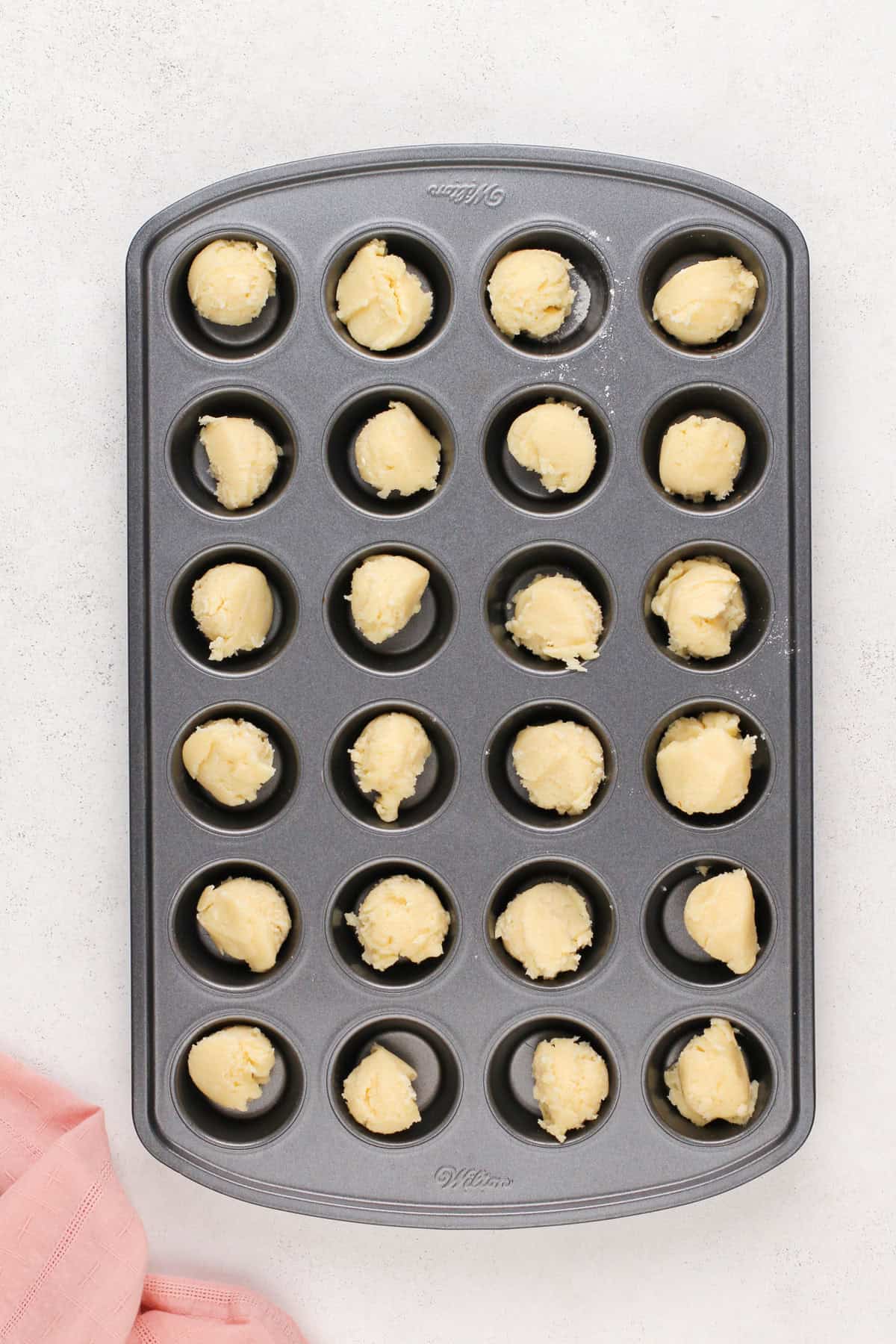 Scoops of tart dough in the wells of a mini muffin tin.