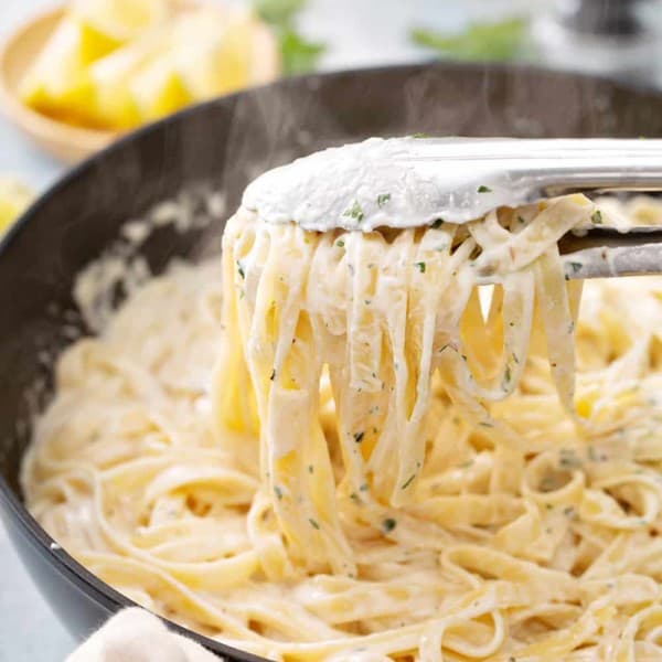 Tongs picking up a serving of fettuccine alfredo out of a skillet