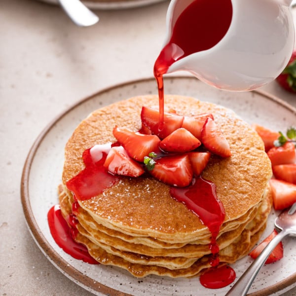 Syrup being poured over a stack of gluten-free pancakes on a white plate.