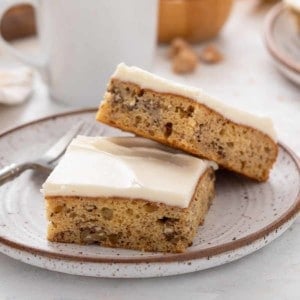 Two banana bars topped with cream cheese frosting on a stoneware plate.