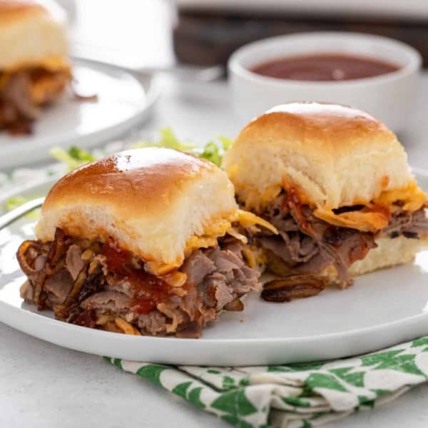 Two cheesy roast beef sliders on a white plate.