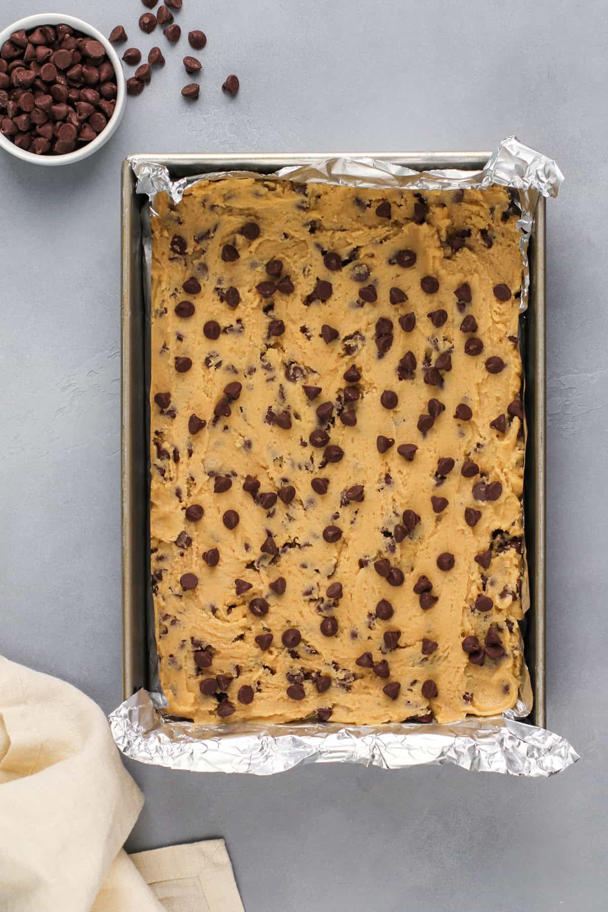 Chocolate chip cookie bar dough pressed into a pan, ready to go in the oven.