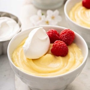 Vanilla pudding in a small white bowl, topped with whipped cream and fresh raspberries