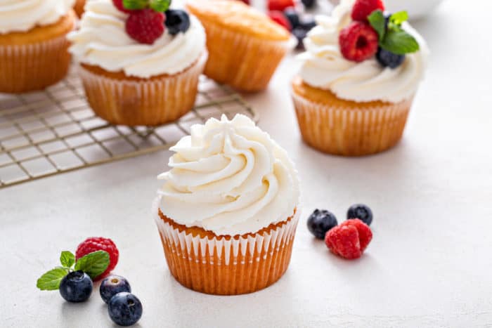 Vanilla cupcake topped with whipped cream frosting on a white countertop.